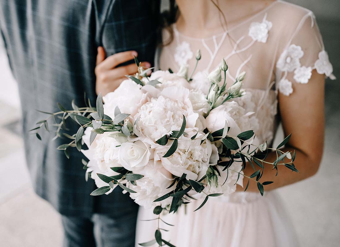 Wedding Insurance - Close-up of a Bouquet in a Bride’s Hands While She is Holding the Arm of the Groom After the Wedding Ceremony
